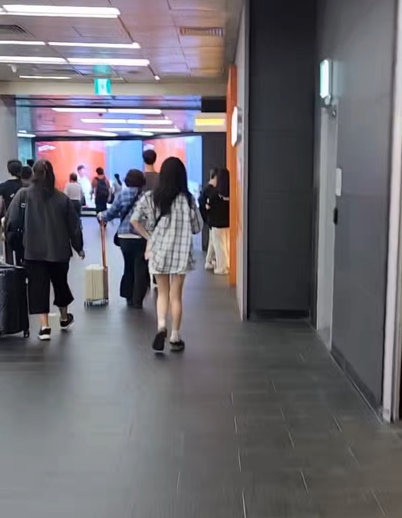 A long underground corridor inside Hongik Univ. Station with travellers walking away from the camera, some pulling suitcases.