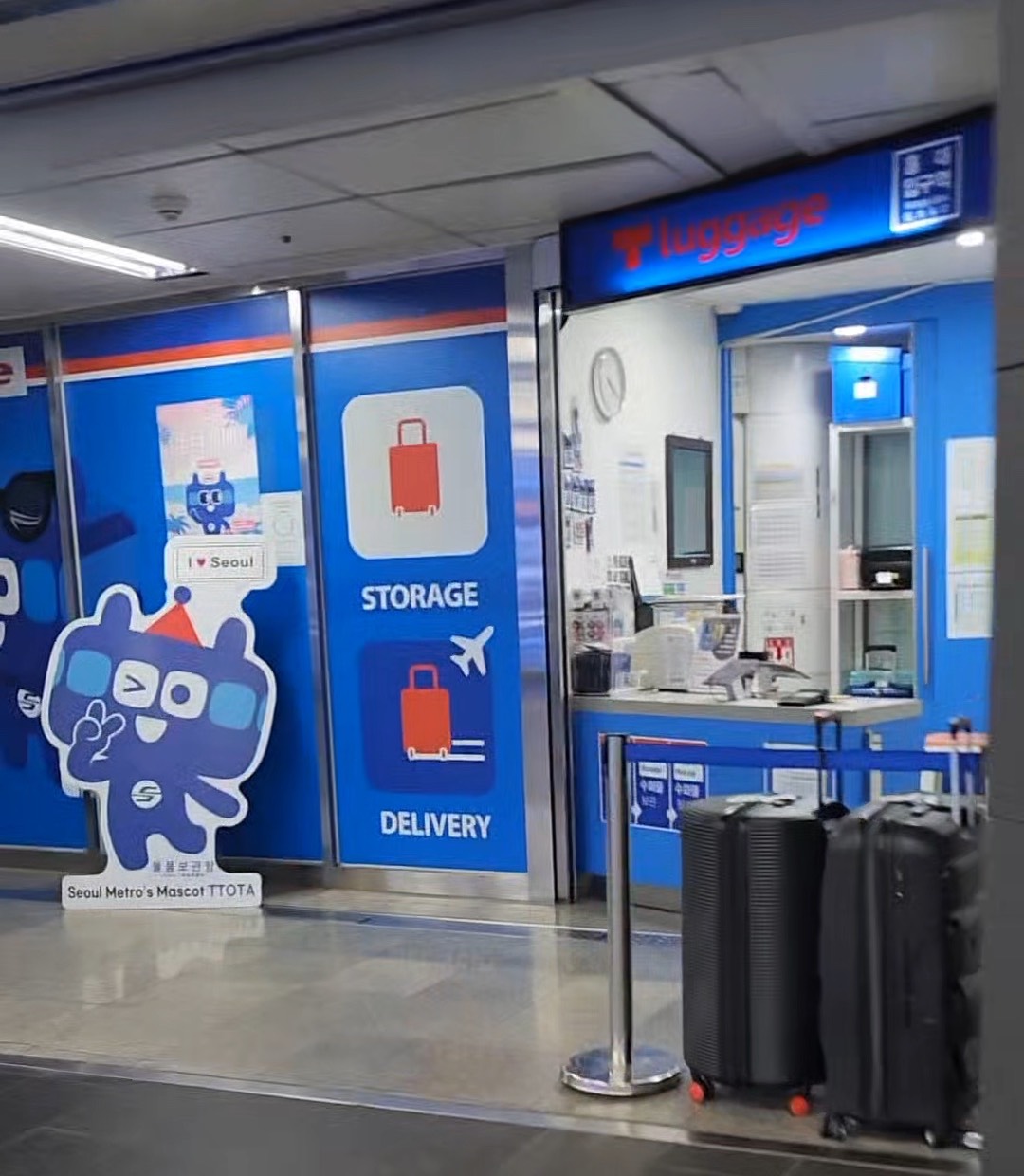 The T-Luggage staffed storage desk inside Hongik Univ. Station, with STORAGE and DELIVERY signage in English and two large suitcases parked at the counter.
