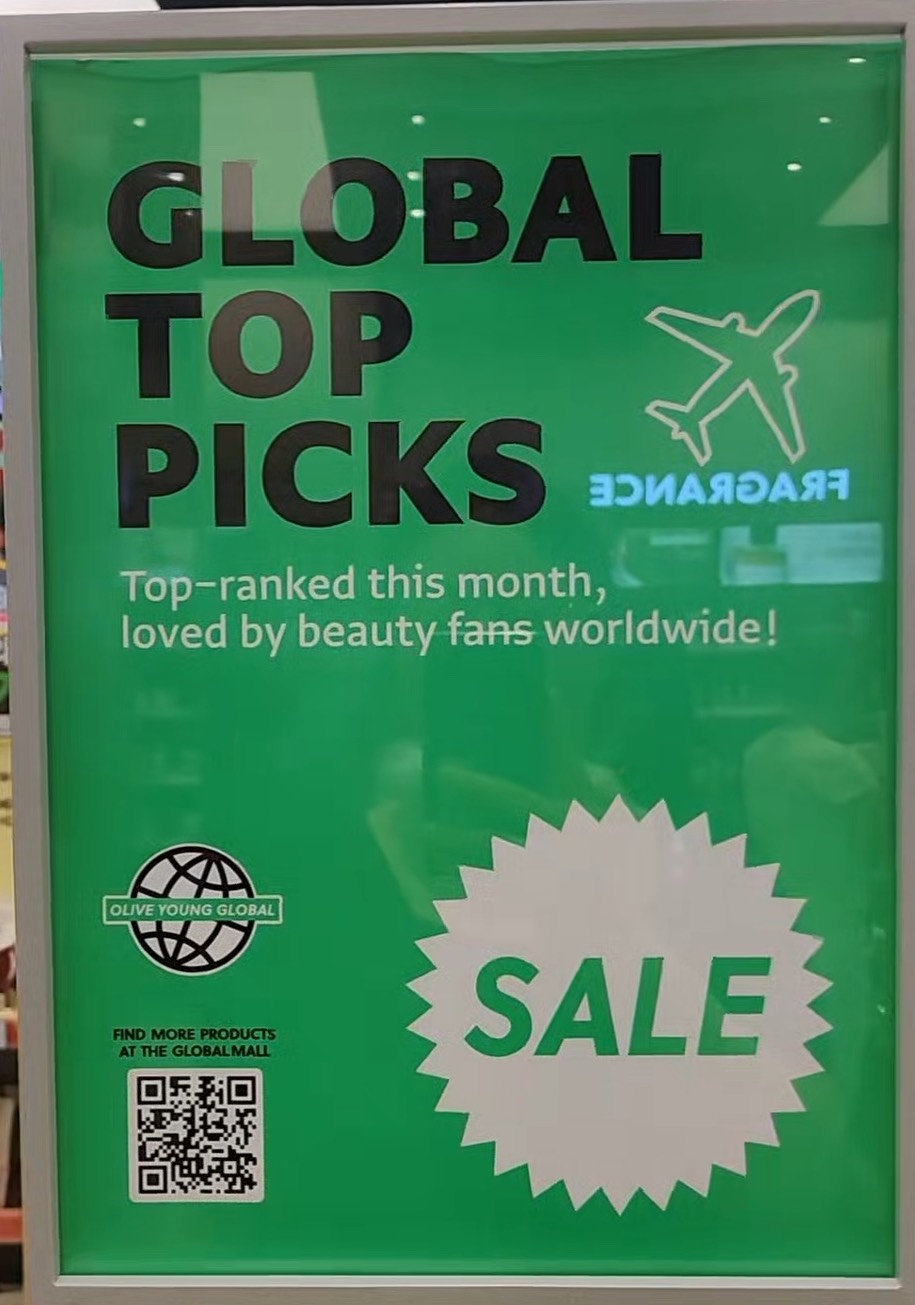 An in-store Olive Young sign in English reading GLOBAL TOP PICKS, top-ranked this month loved by beauty fans worldwide, with a SALE badge and a QR code.