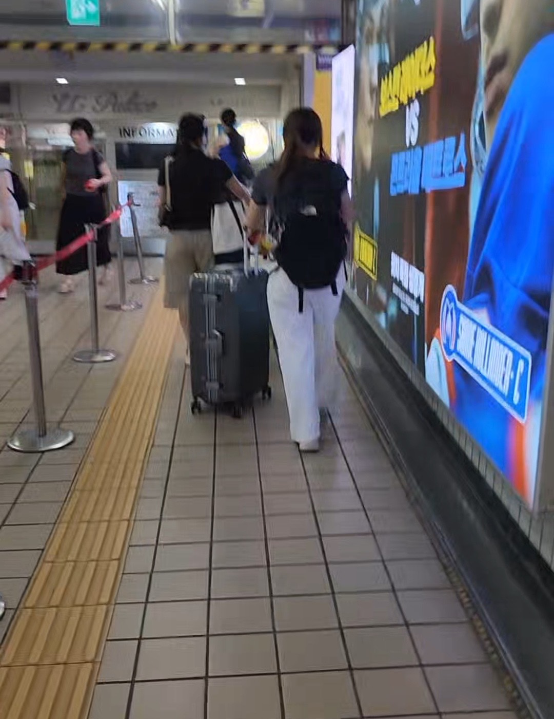 A subway corridor with a traveller pulling a suitcase along it, a yellow tactile paving strip running down the middle of the floor.